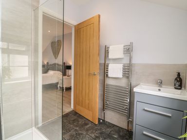 A bathroom with a glass shower screen a wooden door a heated towel rail and a sink with a cabinet at New Inn Apartment in Tholthorpe near Easingwold