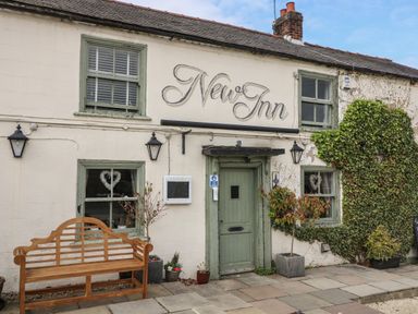 Exterior of a building with a wooden bench in front two windows and a door with plants on the sides at New Inn Apartment Tholthorpe near Easingwold