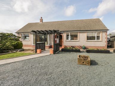 A bungalow with a gravel driveway a black pergola and garden beds at The Croft Bungalow in Plumbland near Aspatria