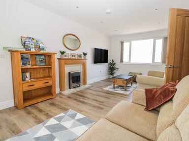 A living room with a beige sofa and armchair wooden bookshelf wooden coffee table fireplace and wall-mounted TV at The Croft Bungalow in Plumbland near Aspatria