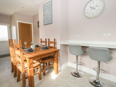 A dining area with a wooden table set for four and two gray bar stools at a counter at The Croft Bungalow in Plumbland near Aspatria