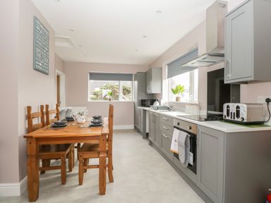 A kitchen with gray cabinets wooden dining table set with black dishes and two windows at The Croft Bungalow Plumbland near Aspatria
