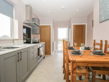A kitchen with grey cabinets a wooden dining table with place settings and wooden chairs at The Croft Bungalow in Plumbland near Aspatria