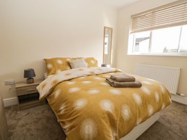 A bedroom with a bed yellow patterned duvet pillows bedside table lamps and window blinds at The Croft Bungalow in Plumbland near Aspatria