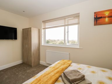 A bedroom with a bed, wooden wardrobe, wall-mounted TV, window with blinds and a radiator at The Croft Bungalow in Plumbland near Aspatria