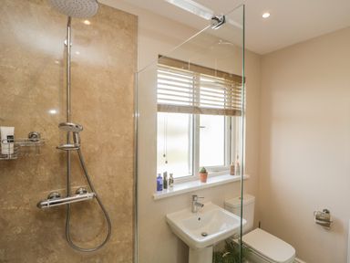 A bathroom with a walk-in shower a pedestal sink a toilet and a window with blinds at The Croft Bungalow in Plumbland near Aspatria