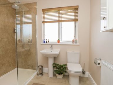 A bathroom with a shower with glass door a pedestal sink a toilet and a window with wooden blinds at The Croft Bungalow in Plumbland near Aspatria