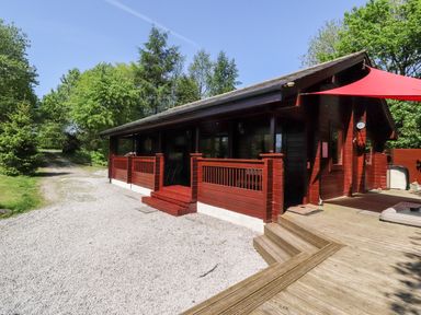 A wooden lodge with a red canopy and surrounding trees at Gisburn Forest Lodge in Tosside near Wigglesworth