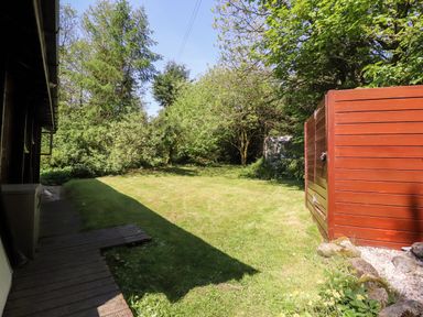A grassy backyard with trees and a red wooden shed near a building with a wooden deck at Gisburn Forest Lodge in Tosside near Wigglesworth