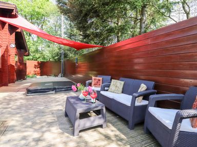 An outdoor seating area with wicker furniture and a hot tub on a wooden deck at Gisburn Forest Lodge Tosside near Wigglesworth
