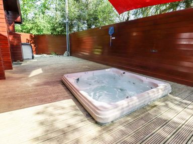 An outdoor wooden deck with a built-in hot tub surrounded by wooden fencing at Gisburn Forest Lodge Tosside near Wigglesworth