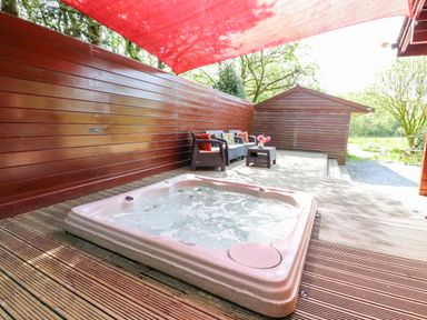 An outdoor wooden deck with a hot tub and seating area under a red canopy at Gisburn Forest Lodge Tosside near Wigglesworth