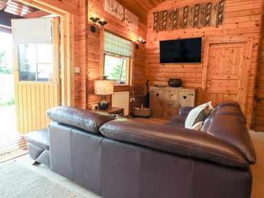 A living room with a brown leather sofa and a wooden cabinet with a wall mounted television at Gisburn Forest Lodge Tosside near Wigglesworth