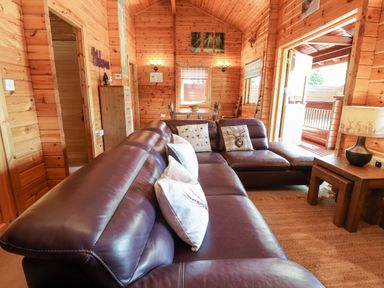 A wooden living room with a brown leather sectional sofa cushions wooden side table with a lamp dining table and chairs by a window at Gisburn Forest Lodge Tosside near Wigglesworth