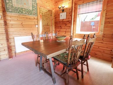 A wooden dining table with six chairs and a bowl on top in a room with wooden walls and a window at Gisburn Forest Lodge in Tosside near Wigglesworth