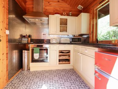 A kitchen with white cabinets a stainless steel oven and range hood a red Montpellier fridge and patterned tiled floor at Gisburn Forest Lodge Tosside near Wigglesworth