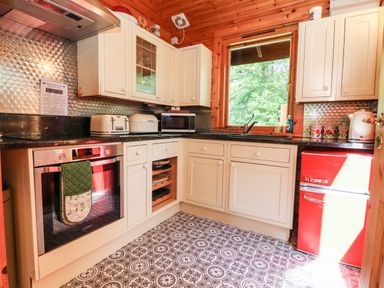 A kitchen with white cabinets a window a red refrigerator and patterned floor at Gisburn Forest Lodge Tosside near Wigglesworth