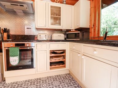 A kitchen with white cabinets a microwave a toaster an oven and a window showing trees at Gisburn Forest Lodge Tosside near Wigglesworth