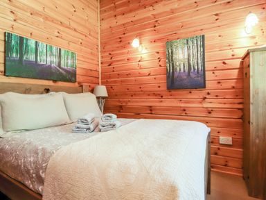 A bedroom with a double bed wooden walls and two landscape paintings at Gisburn Forest Lodge Tosside near Wigglesworth