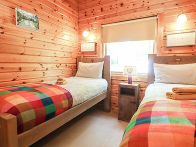 A bedroom with two single beds wooden walls and a window with a roller blind at Gisburn Forest Lodge Tosside near Wigglesworth