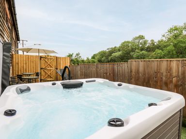 An outdoor hot tub with bubbling water next to a wooden fence and patio furniture at Bluebell Cottage in Pembridge