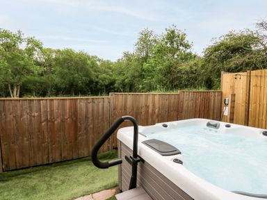 An outdoor hot tub with handrails next to a wooden fence and trees in the background at Bluebell Cottage in Pembridge