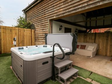 An outdoor hot tub with steps next to a covered seating area with a couch at Bluebell Cottage in Pembridge
