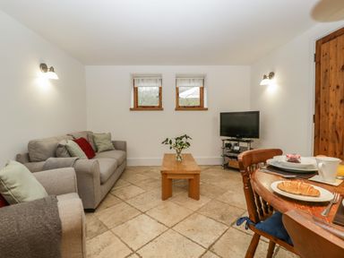 A living room with beige tiled floor sofa coffee table tv and dining table with croissant at Bluebell Cottage in Pembridge