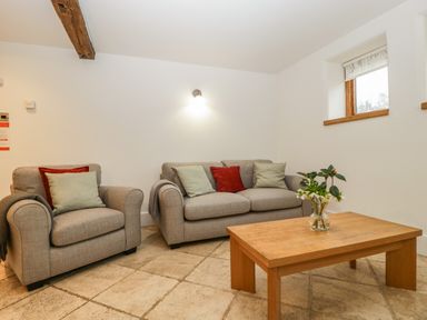 A living room with a grey armchair and sofa with cushions and a wooden coffee table with a vase of flowers at Bluebell Cottage in Pembridge