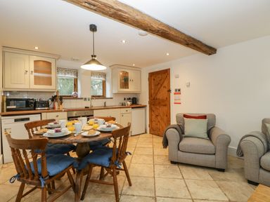 A kitchen and dining area with wooden furniture and upholstered chairs at Bluebell Cottage in Pembridge