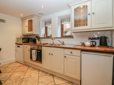 A kitchen with white cabinets wooden countertop and tiled floor with oven sink microwave and kettle at Bluebell Cottage in Pembridge