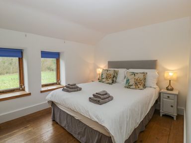 A bedroom with a double bed bedside tables and windows with blue blinds at Bluebell Cottage in Pembridge