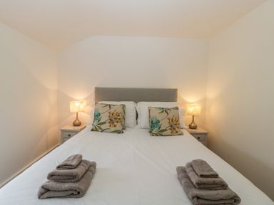 A bedroom with a double bed two floral pillows two bedside tables with lamps and folded towels at Bluebell Cottage in Pembridge