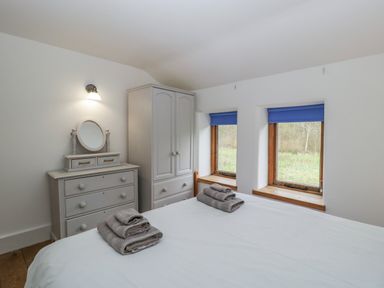 A bedroom with a bed folded towels two windows with blue blinds a chest of drawers and a wardrobe at Bluebell Cottage in Pembridge