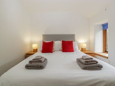 A bedroom with a double bed with red pillows and towels on the bed at Bluebell Cottage in Pembridge