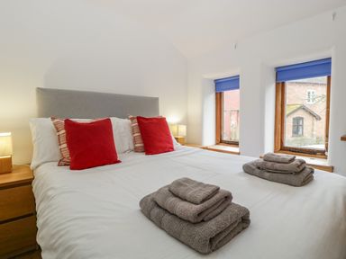 A bedroom with a double bed with red and striped pillows and folded towels by the windows at Bluebell Cottage in Pembridge