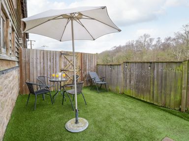 An outdoor patio with artificial grass a table with four chairs a patio umbrella and a wooden fence at Bluebell Cottage in Pembridge