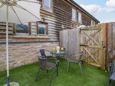 A small outdoor patio with a round glass table four chairs a white umbrella and wooden fencing at Bluebell Cottage in Pembridge