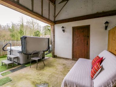A covered outdoor area with a hot tub chair and a sofa with cushions at Bluebell Cottage in Pembridge