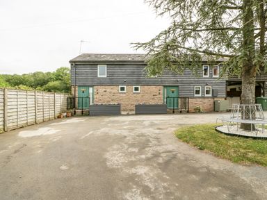 A driveway with a two door stone and wood exterior building and a tree with a round metal bench at Bluebell Cottage in Pembridge