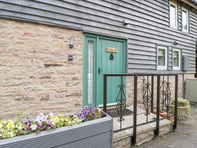 A green door with a sign bluebell cottage on a stone and wood house exterior with flower boxes and a black iron railing at Bluebell Cottage in Pembridge