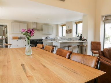 A dining area with a wooden table and leather chairs next to a kitchen with white cabinets and bar stools at Pheasant's Roost in Lelley near Burton Pidsea