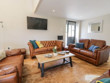 A living room with brown leather sofas a wooden coffee table and a wall-mounted TV at Pheasant's Roost in Lelley near Burton Pidsea