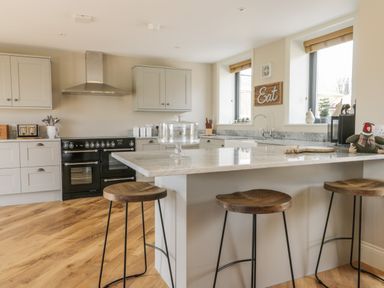 A kitchen with wooden stools at a marble island countertop and black stove at Pheasant's Roost in Lelley near Burton Pidsea