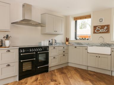 A kitchen with black stove white farmhouse sink wooden floor and eat sign at Pheasant's Roost in Lelley near Burton Pidsea