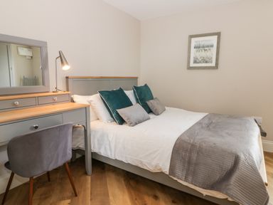 A bedroom with a bed and pillows beside a desk with a mirror and lamp at Pheasant's Roost in Lelley near Burton Pidsea
