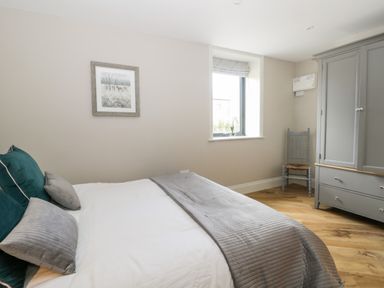 A bedroom with a bed grey pillows a wardrobe a chair and a window at Pheasant's Roost in Lelley near Burton Pidsea
