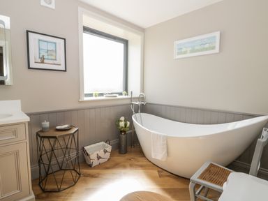 A bathroom with a freestanding bathtub a wooden chair a small table and wall art at Pheasant's Roost in Lelley near Burton Pidsea
