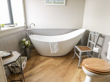 A bathroom with a freestanding bathtub a chair a toilet and a side table at Pheasant's Roost in Lelley near Burton Pidsea
