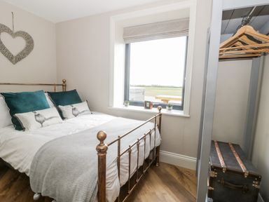 A bedroom with a metal bed frame green pillows and an open wardrobe with hangers at Pheasant's Roost in Lelley near Burton Pidsea